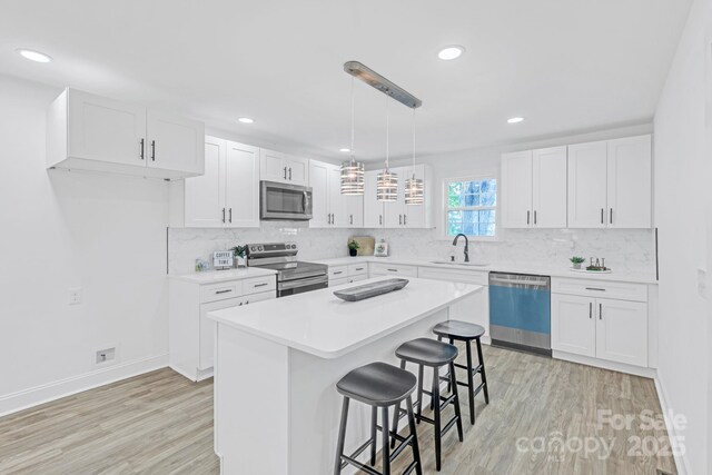 kitchen with light wood-style floors, a breakfast bar area, white cabinets, a sink, and appliances with stainless steel finishes