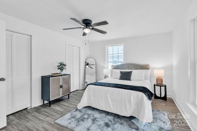 bedroom with two closets, ceiling fan, baseboards, and wood finished floors