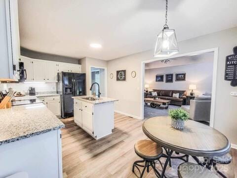6231 Kentwood Dr, Kannapolis, NC 28081 - kitchen with black fridge with ice dispenser, light wood-style floors, white cabinets, stove, and an island with sink