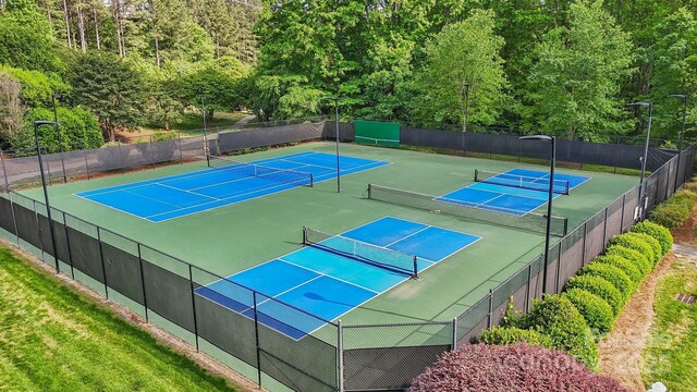 view of sport court featuring fence and a wooded view
