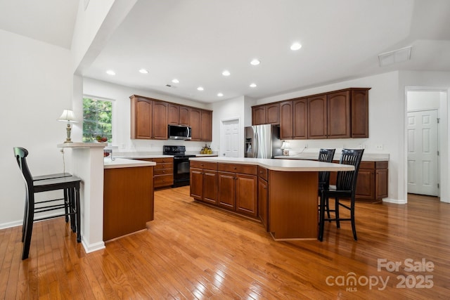 109 Braxton Gate Ct, Mount Holly, NC 28120 - kitchen with appliances with stainless steel finishes, a breakfast bar area, light wood-style flooring, recessed lighting, and light countertops