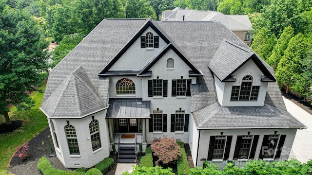 french provincial home featuring brick siding, roof with shingles, and stucco siding