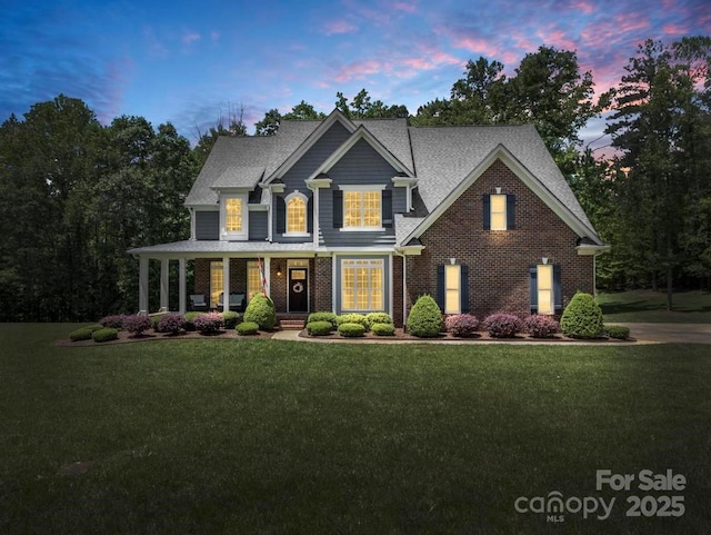 view of front facade with brick siding, a shingled roof, covered porch, and a front yard