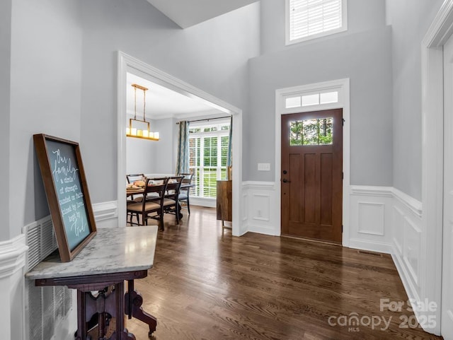 foyer with visible vents, wainscoting, a decorative wall, dark wood-style floors, and a notable chandelier