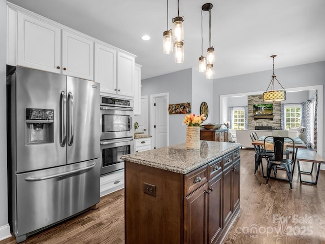 kitchen with white cabinets, light stone counters, stainless steel appliances, pendant lighting, and dark wood-style floors