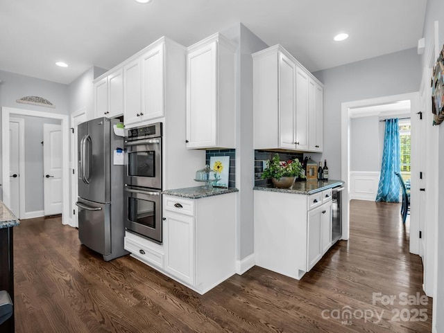 kitchen featuring dark wood-style flooring, appliances with stainless steel finishes, white cabinets, dark stone countertops, and wine cooler