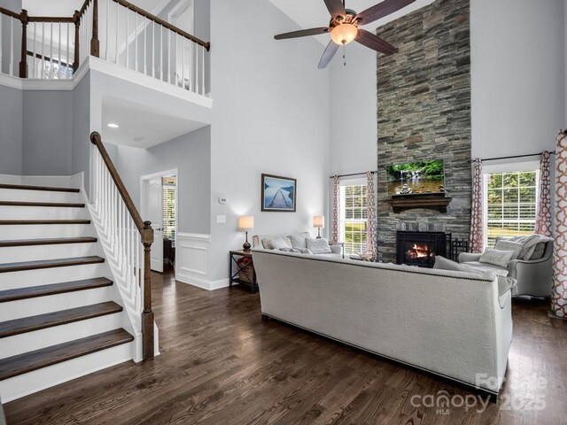 living room featuring a high ceiling, a fireplace, a ceiling fan, and dark wood finished floors