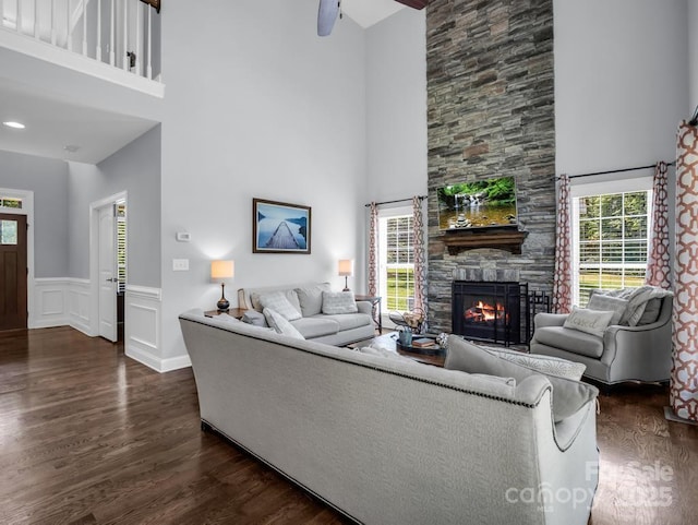 living area with a fireplace, wainscoting, dark wood-style floors, and a towering ceiling