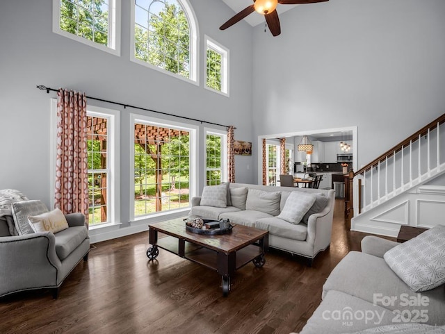 living room with stairway, a high ceiling, dark wood-style floors, and ceiling fan