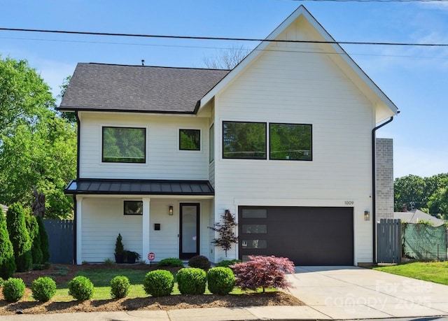 view of front of house featuring a standing seam roof, fence, concrete driveway, and a garage