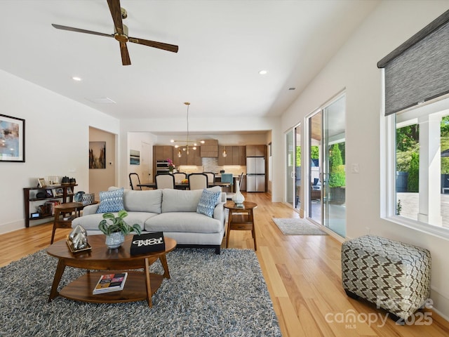 living room featuring recessed lighting, baseboards, light wood finished floors, and ceiling fan with notable chandelier