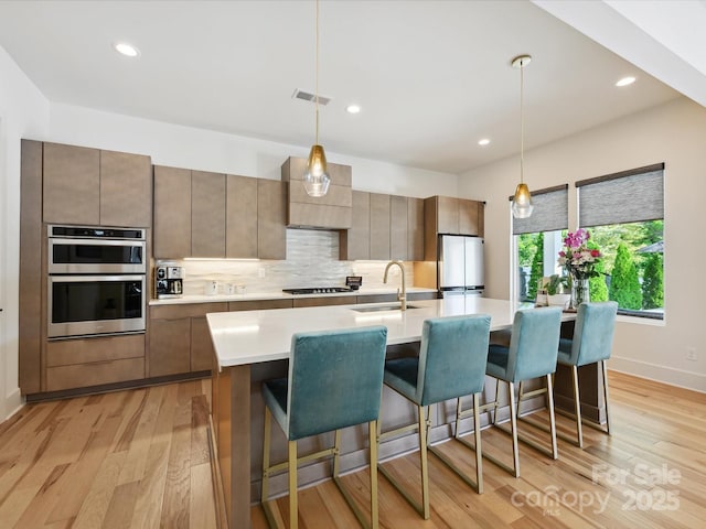 kitchen featuring light countertops, a sink, light wood-style flooring, backsplash, and stainless steel appliances