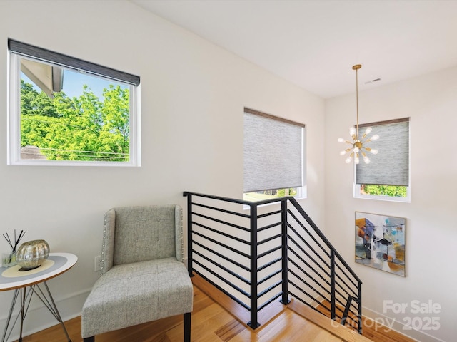 living area with a chandelier, a wealth of natural light, an upstairs landing, and wood finished floors