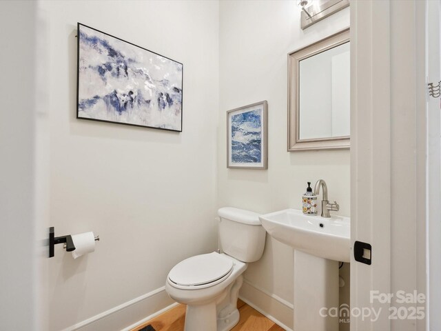 half bathroom featuring toilet, baseboards, a sink, and wood finished floors