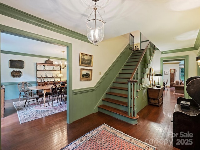 staircase with wood-type flooring, wainscoting, crown molding, and a chandelier