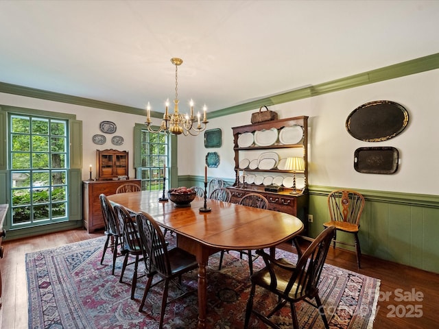 dining space featuring a chandelier, a wainscoted wall, ornamental molding, and wood finished floors