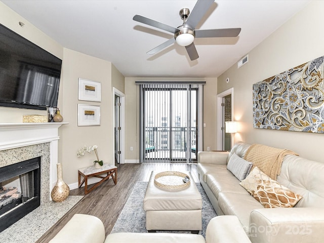 living area with ceiling fan, visible vents, wood finished floors, baseboards, and a premium fireplace
