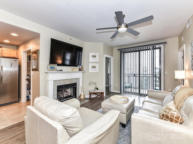 living area with baseboards, a ceiling fan, a glass covered fireplace, and wood finished floors