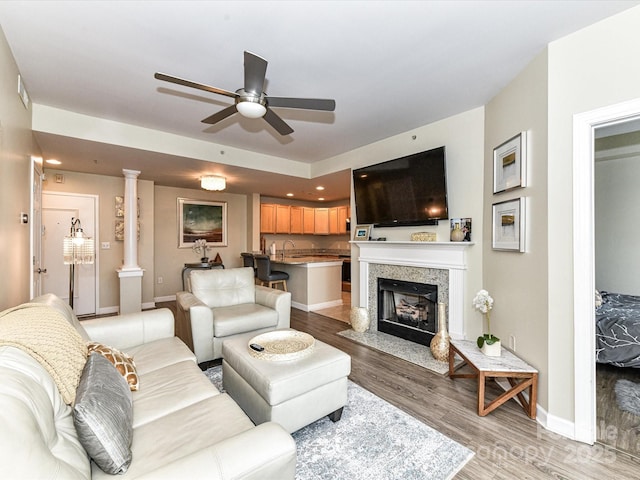 living area with a fireplace with flush hearth, baseboards, ceiling fan, and light wood-style flooring
