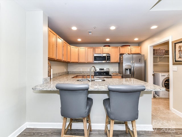 kitchen featuring washer / dryer, a peninsula, light brown cabinets, a sink, and appliances with stainless steel finishes