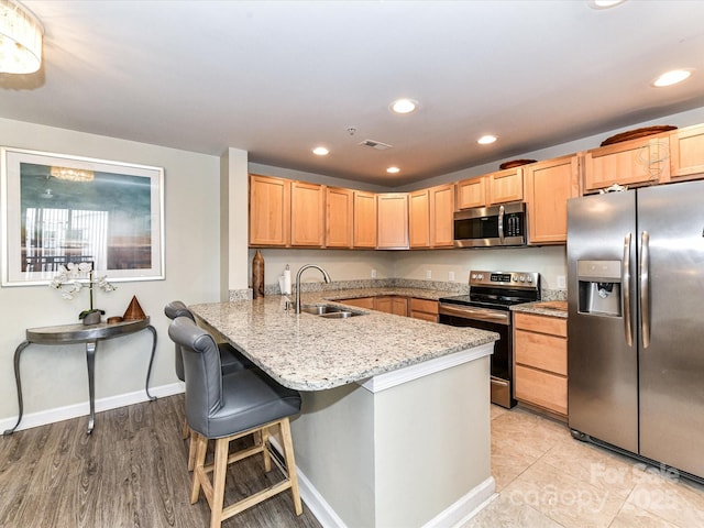 kitchen featuring visible vents, a peninsula, light stone countertops, a sink, and stainless steel appliances