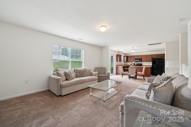 living area featuring baseboards, plenty of natural light, visible vents, and light colored carpet