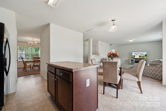 kitchen with decorative light fixtures, dark brown cabinets, freestanding refrigerator, open floor plan, and an inviting chandelier
