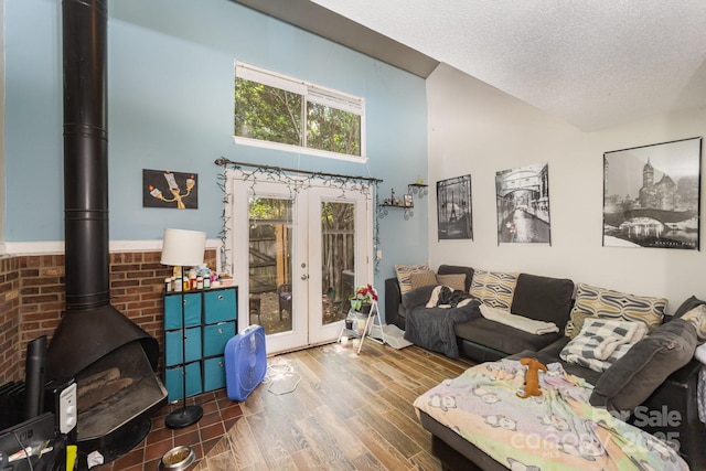living area featuring french doors, a wood stove, wood finished floors, a textured ceiling, and a towering ceiling