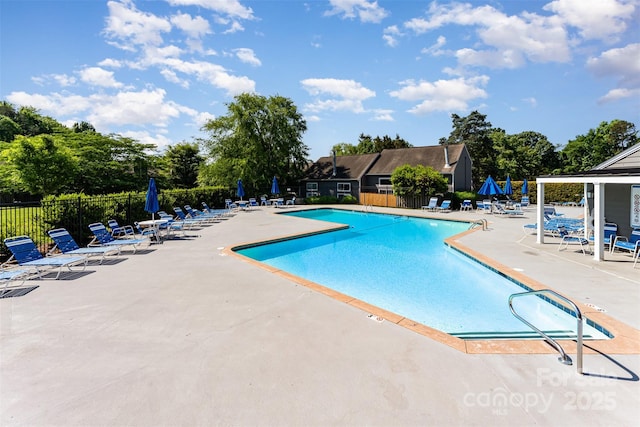 community pool with a patio, fence, and view of wooded area