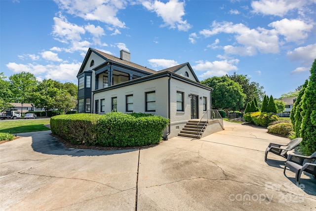 view of side of property featuring a chimney, brick siding, and a patio