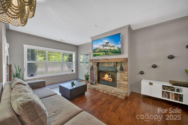 living room with a notable chandelier, a stone fireplace, baseboards, wood finished floors, and ornamental molding