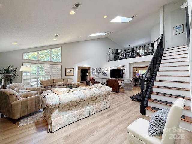 living area featuring light wood-style floors, high vaulted ceiling, a skylight, and stairs