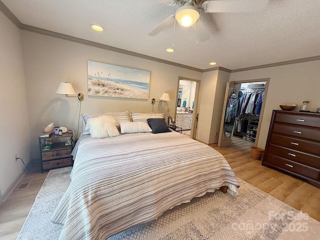bedroom featuring crown molding, a walk in closet, a ceiling fan, and light wood-style flooring