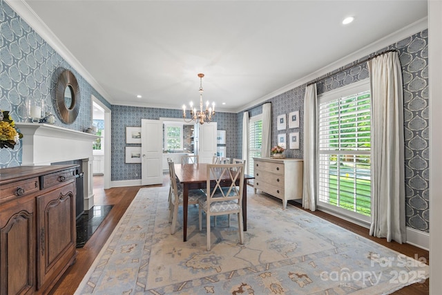 dining room with wallpapered walls, ornamental molding, a chandelier, wood finished floors, and baseboards