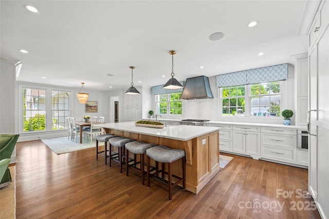 kitchen featuring wall chimney range hood, wood finished floors, light countertops, a center island, and white cabinets