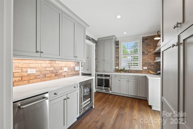 kitchen featuring appliances with stainless steel finishes, wine cooler, backsplash, a sink, and dark wood-style floors