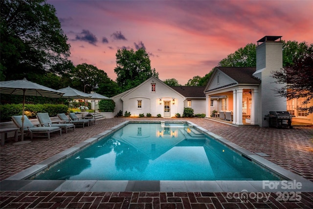 pool at dusk featuring a patio area, an outdoor pool, and area for grilling