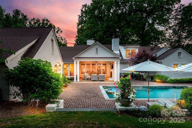 back of house with a patio area, outdoor lounge area, a chimney, a hot tub, and an outdoor pool