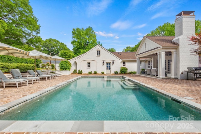 swimming pool with a patio, grilling area, and ceiling fan