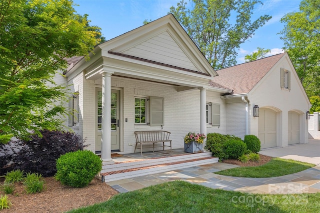 neoclassical / greek revival house with covered porch, brick siding, a garage, driveway, and roof with shingles