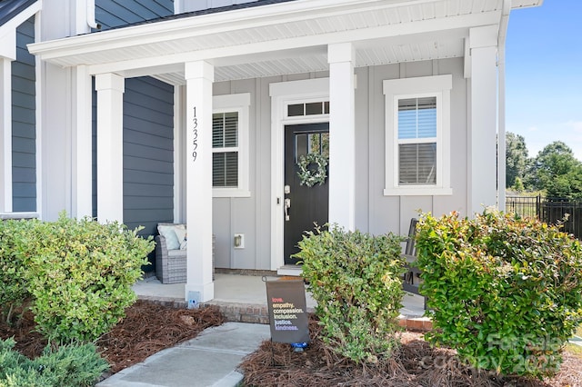 view of exterior entry with covered porch, board and batten siding, and fence