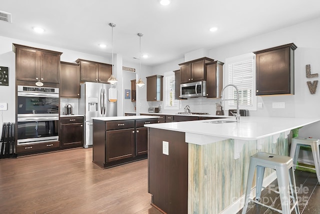 kitchen featuring appliances with stainless steel finishes, a sink, dark brown cabinets, a peninsula, and light countertops