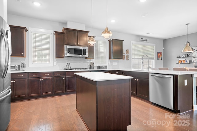 kitchen featuring stainless steel appliances, a peninsula, a sink, light wood-type flooring, and plenty of natural light