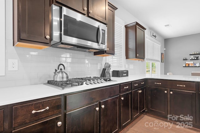 kitchen featuring stainless steel appliances, backsplash, light countertops, and dark brown cabinetry