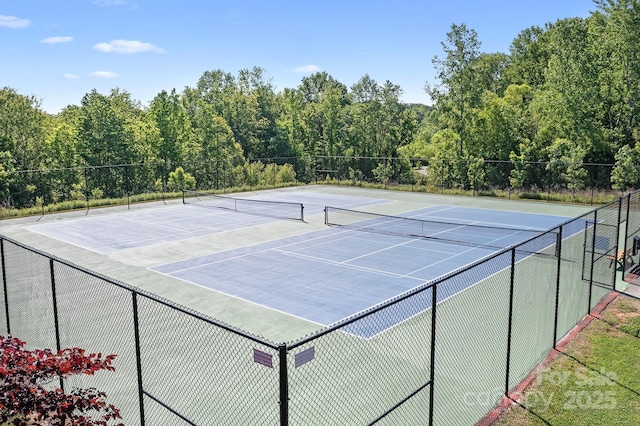 view of tennis court with fence, community basketball court, and a forest view