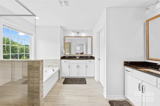 bathroom with a garden tub, visible vents, two vanities, and a sink