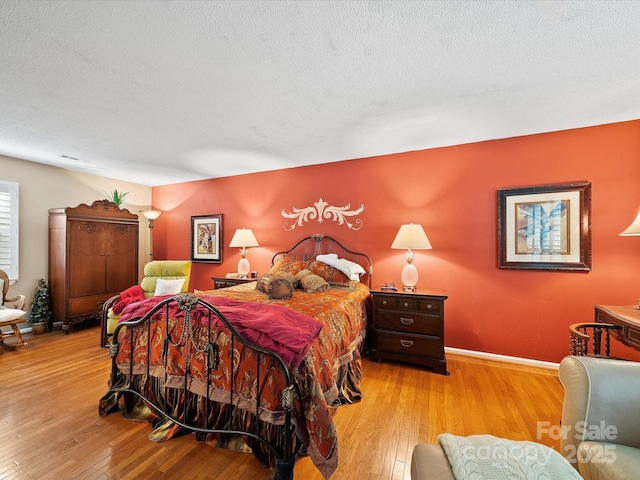 bedroom with light wood-type flooring, baseboards, and a textured ceiling