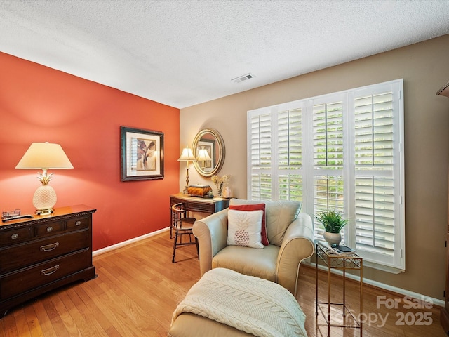 living area featuring baseboards, light wood-style floors, and a textured ceiling