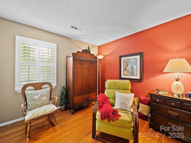 living area featuring a textured ceiling, wood finished floors, and baseboards