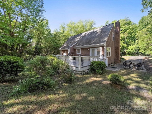 rear view of house featuring a wooden deck, a chimney, roof with shingles, and a patio area